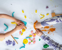 Picture of 2 sets of children's hands playing with playdough on a table.