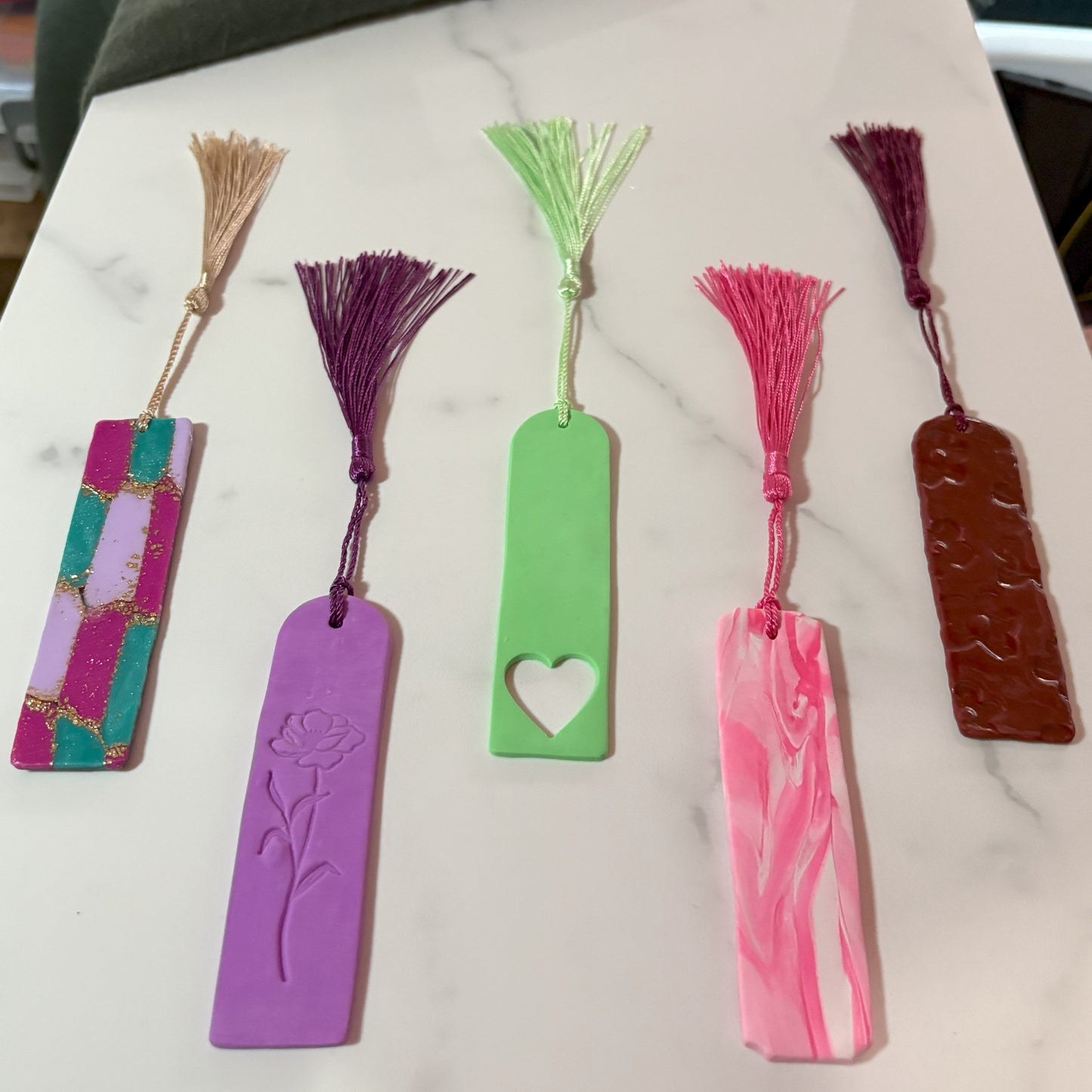 Set of five colorful bookmarks with tassels on a marble surface