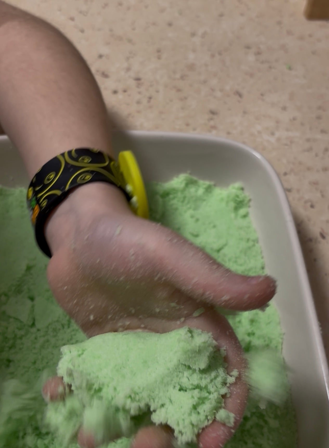 A child's hand squishing a ball of green kinetic sand through his fingers