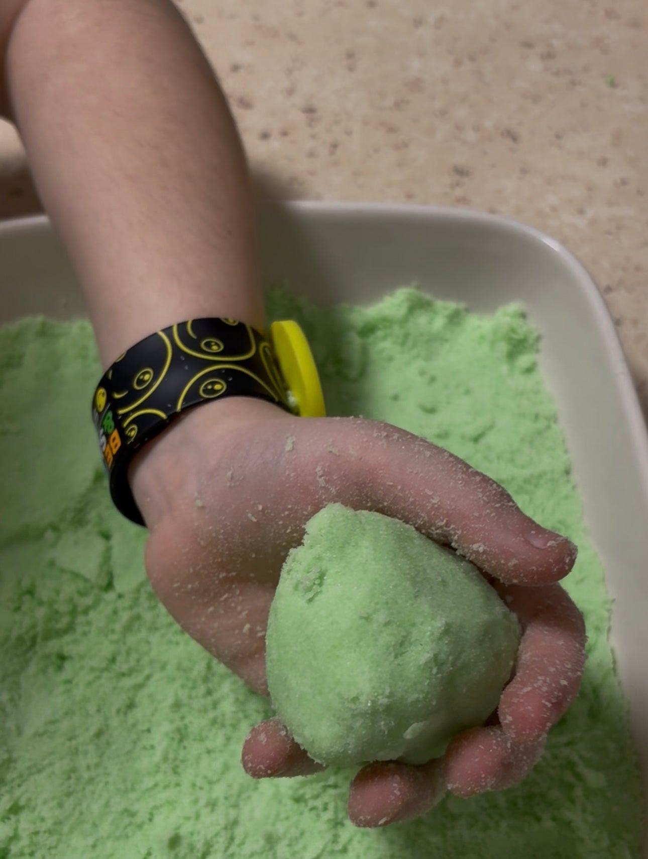 A child's hand holding a ball he has made out of green kinetic sand