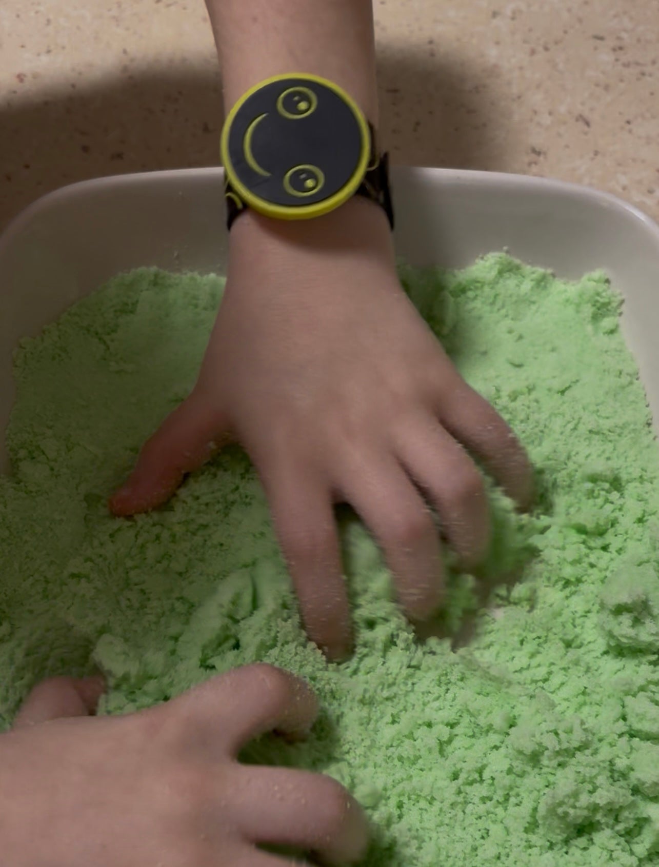 Two hands playing with green kinetic sand