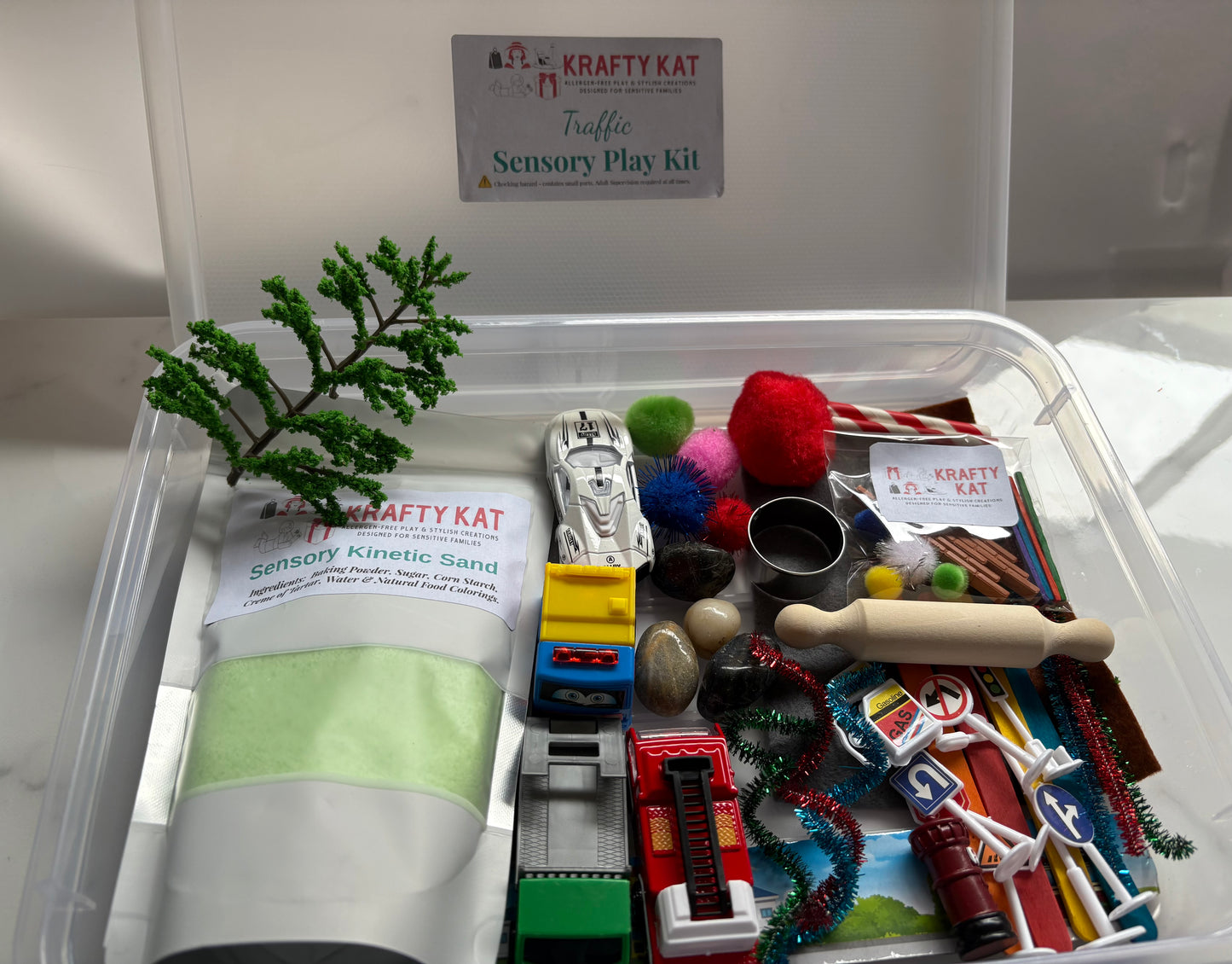 Krafty Kat traffic sensory play kit with toys and kinetic sand in a clear container.
