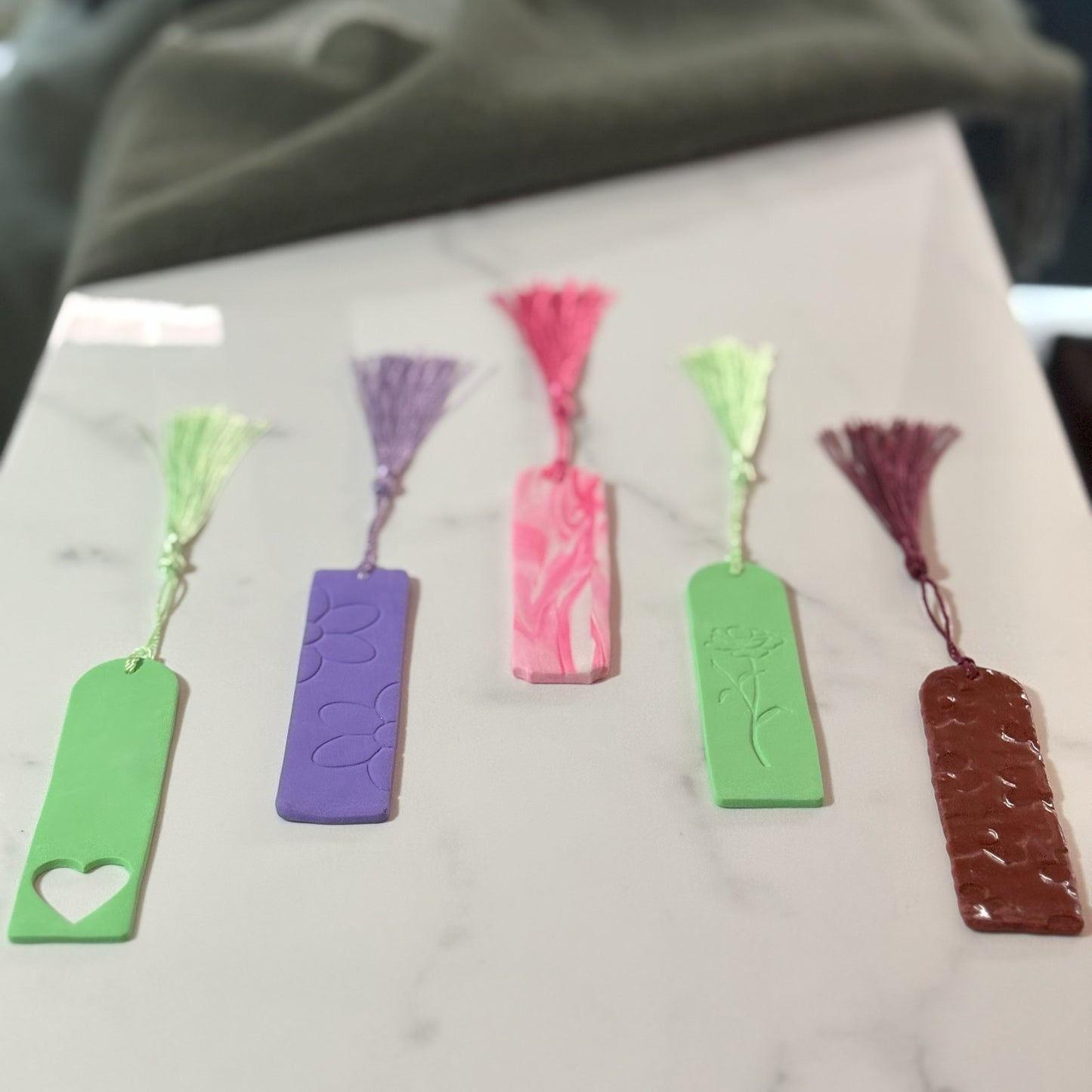 Five colorful bookmarks with tassels on a marble surface