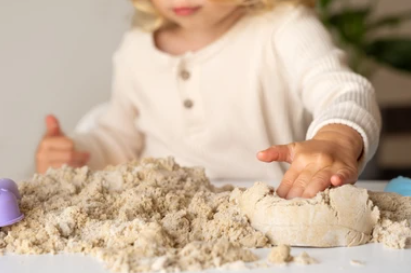 A young child is squishing a mound of kinetic sand  on the tabletop