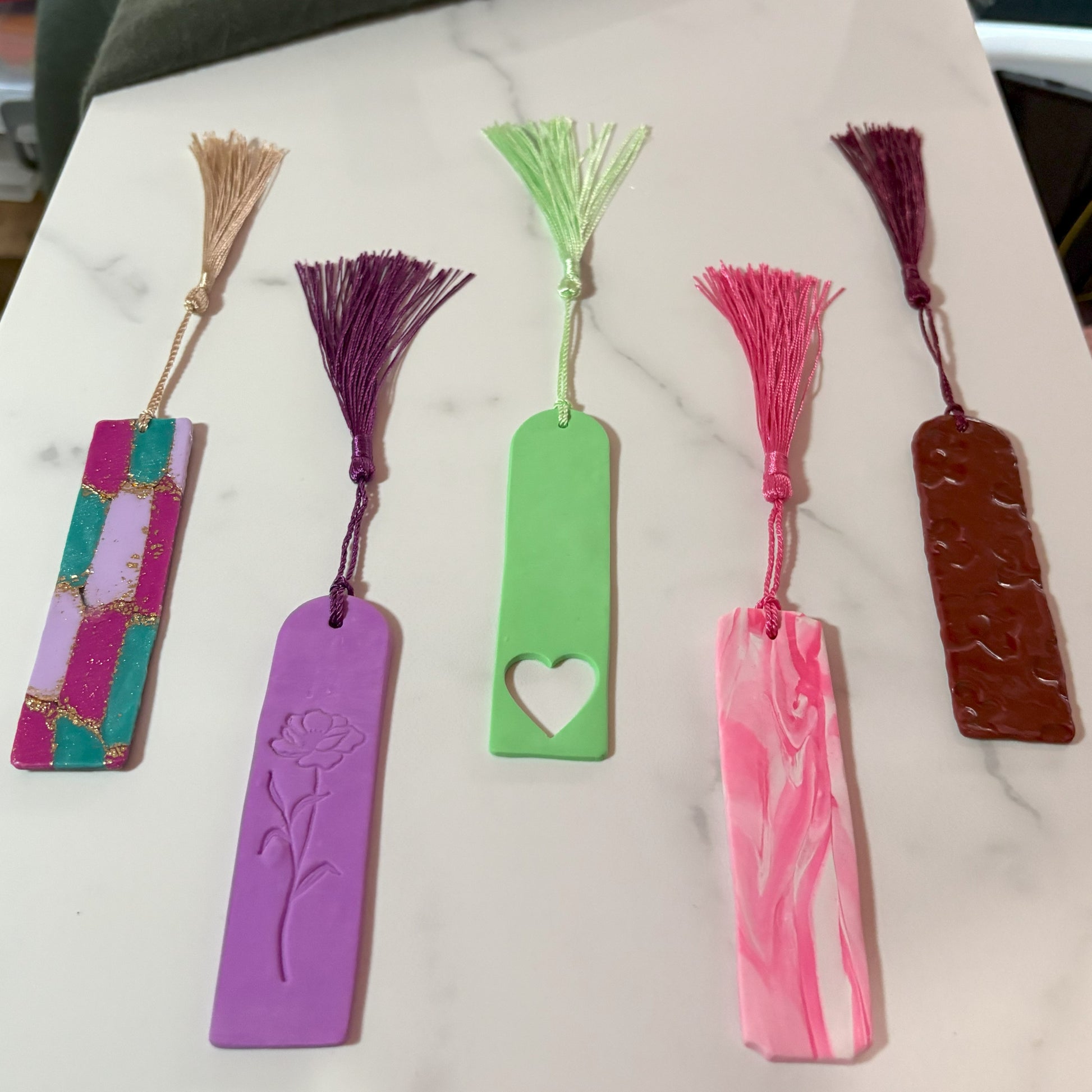 Set of five colorful bookmarks with tassels on a marble surface