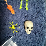 Some handmade purple allergen-free kinetic sand with a few Halloween figurines on top with a clear plastic scoop