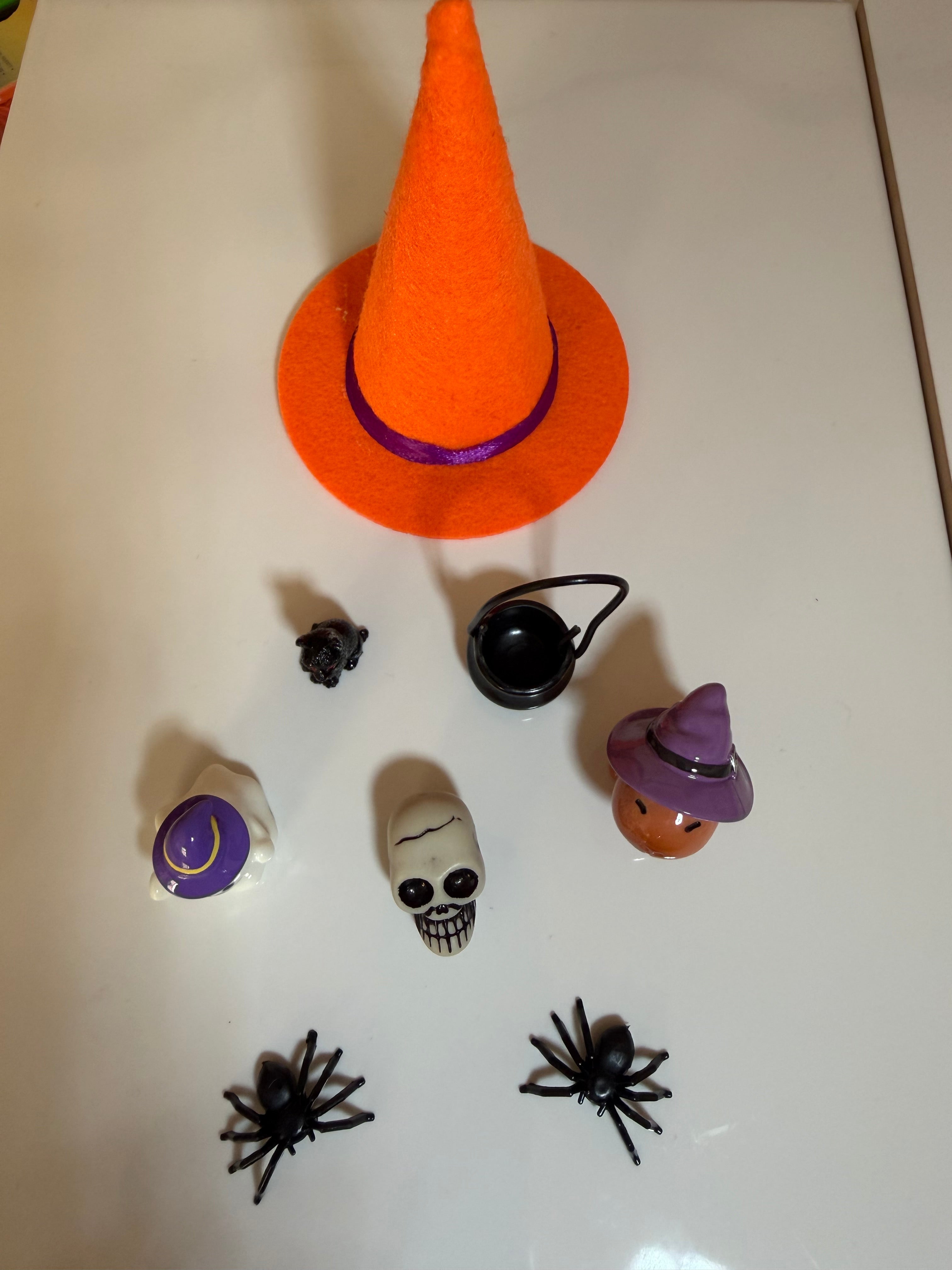 A collection of Halloween miniatures such as a mini orange witches hat, cauldron, black cat, skeleton head & spiders